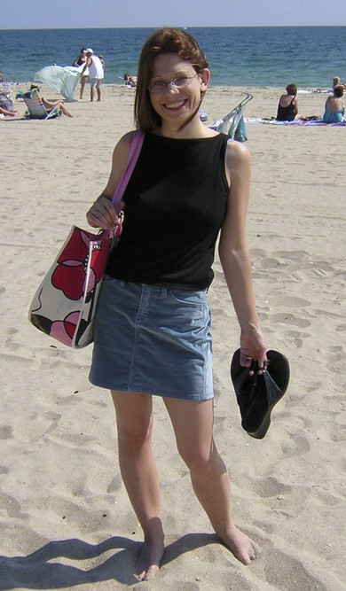 Junge Frau in Jeansrock und schwarzem Shirt steht am Strand.