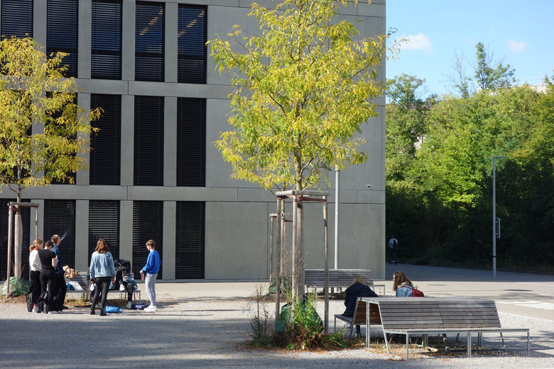 Schüler*innen stehen in einer Gruppe auf dem Pausenplatz vor dem Schulhaus.