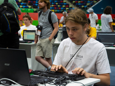Junger Mann mit langen Haaren und Bart sitzt vor Computer und tippt auf der Tastatur.