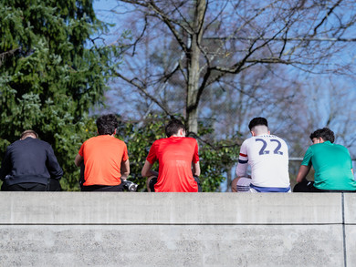 Fünf Jugendliche sitzen auf einer Mauer, wir sehen sie von hinten.