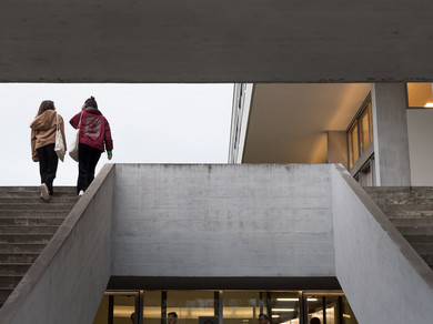 Zwei Schüler*innen gehen eine Betontreppe hoch. Man sieht sie von hinten.