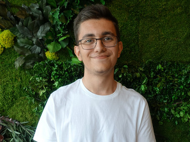 Junger Mann mit Brille vor einer Wand mit Moos.