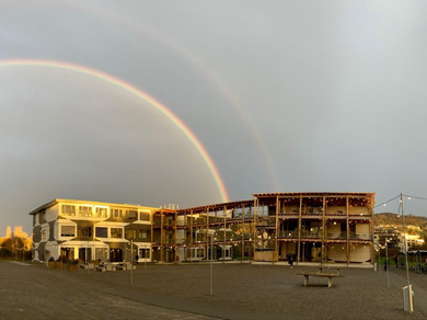 Gebäude mit einem sehr grossen doppelten Regenbogen im Hintergrund.