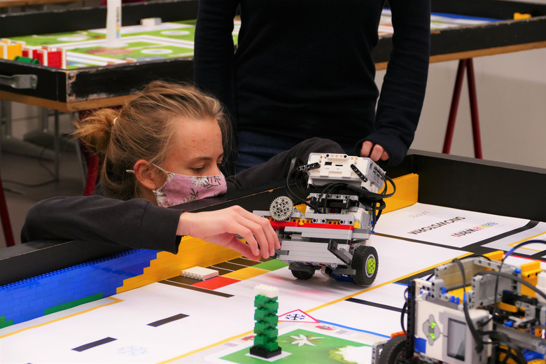 Eine junge Frau stellt einen Roboter auf einem Spielfeld auf einem Tisch auf. 