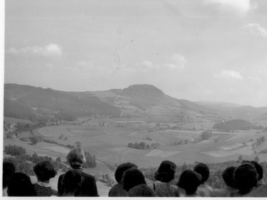 Schwarzweiss-Foto: Kinderköpfe von hinten bei einem Aussichtspunkt mit Blick auf die Berge.