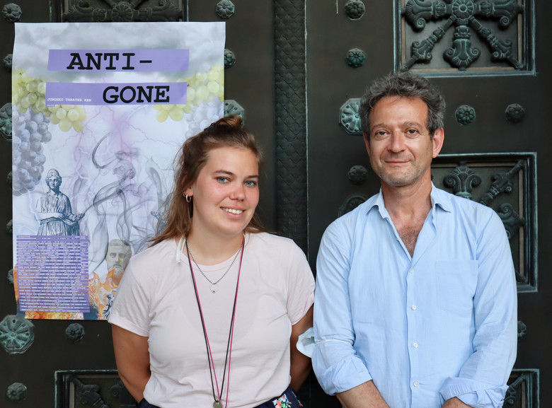 Junge Frau steht neben älterem Mann vor einem Poster mit dem Schriftzug «Anti-gone».