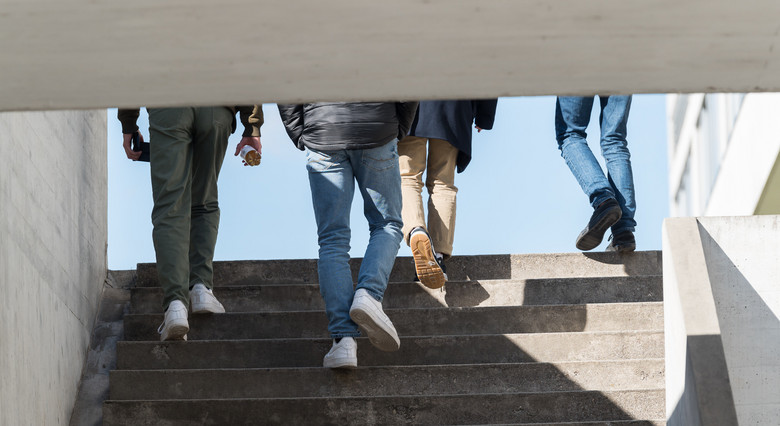 Schüler gehen eine Betontreppe hinauf. Man sieht sie von hinten.