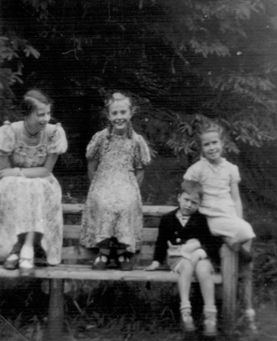 Schwarzweiss-Foto: Drei Mädchen und ein Junge sitzen auf einem Bank und schauen in die Kamera.