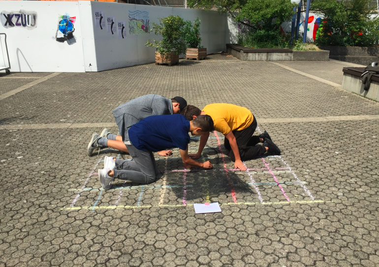 Schüler malen mit Strassenkreide auf den Boden.
